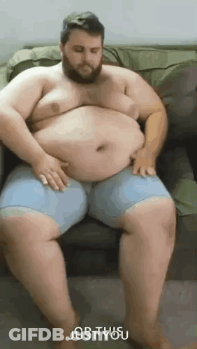 A Very Fat Man With A Beard Is Sitting On A Couch With His Hands On His Belly . GIF