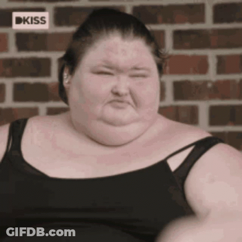 A Very Fat Woman Wearing A Black Tank Top Is Sitting In Front Of A Brick Wall GIF