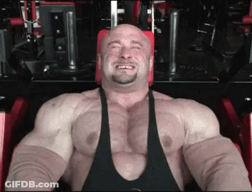 A Very Muscular Man Is Sitting On A Machine In A Gym . GIF