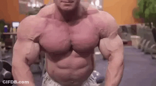 A Very Muscular Man Is Standing In A Gym With His Arms Outstretched . GIF