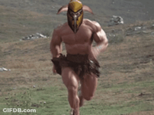 A Very Muscular Man With A Helmet On His Head Is Running Through A Grassy Field . GIF