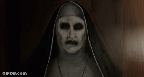 A Very Scary Nun With A Mustache Is Standing In A Dark Room . GIF