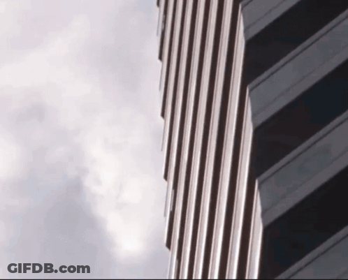 A Very Tall Building With A Cloudy Sky Behind It GIF