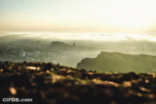 A View Of A City From A Hill With The Sun Shining Through The Clouds GIF
