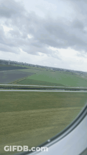 A View Of A Field From An Airplane Window With A Cloudy Sky GIF