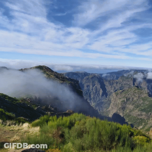 A View Of A Mountain Range With A Blue Sky And Clouds In The Background GIF