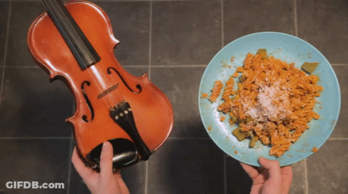 A Violin Next To A Plate Of Pasta With Cheese GIF