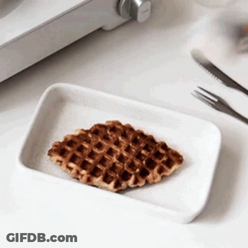 A Waffle On A White Plate Next To A Fork And Knife . GIF