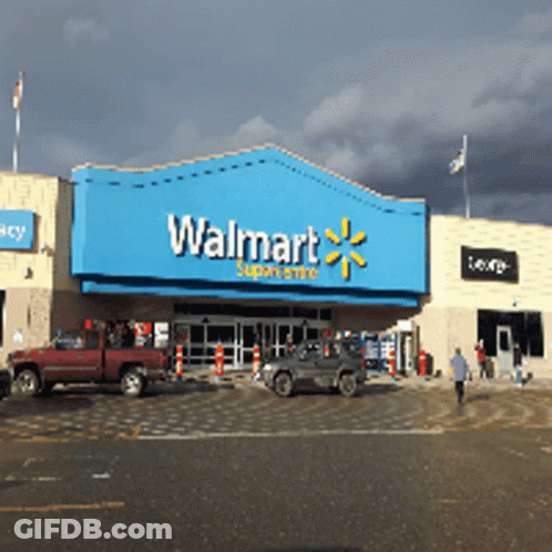 A Walmart Store With Cars Parked In Front Of It On A Cloudy Day GIF