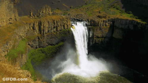 A Waterfall In The Middle Of A Canyon With A Few Trees In The Background GIF