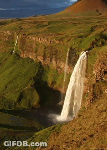 A Waterfall In The Middle Of A Grassy Valley GIF