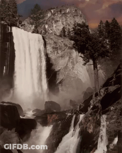 A Waterfall Is Surrounded By Rocks And Trees And A Mountain In The Background GIF
