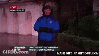 A Weatherman In A Blue Jacket Is Standing In Front Of A Building In The Dark . GIF