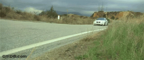 A White Bmw Is Driving Down A Road GIF