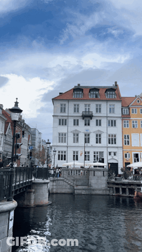 A White Building With A Red Roof Sits Next To A River GIF