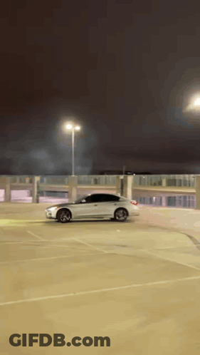 A White Car Is Doing A Stunt In A Parking Lot At Night GIF