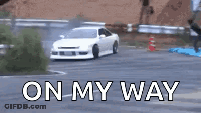 A White Car Is Drifting Down A Road With The Words `` On My Way '' Written On The Bottom . GIF