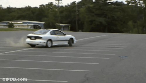 A White Car Is Drifting In A Parking Lot With A Building In The Background GIF