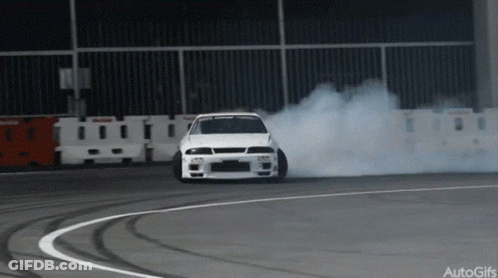 A White Car Is Drifting On A Track And Smoke Is Coming Out Of The Tire GIF