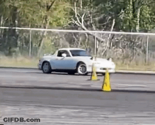 A White Car Is Drifting On A Track Next To Yellow Cones . GIF