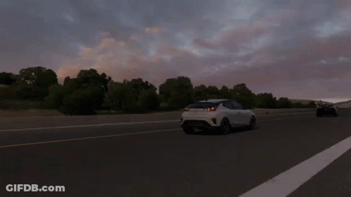 A White Car Is Driving Down A Highway With Trees In The Background GIF