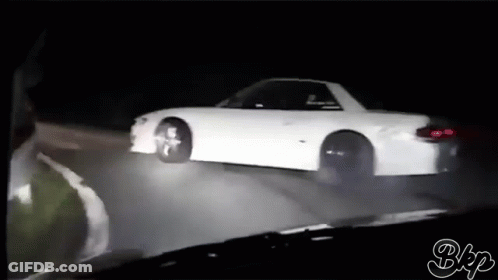 A White Car Is Driving Down A Road At Night GIF
