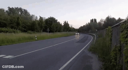 A White Car Is Driving Down A Road With A Fence In The Background GIF