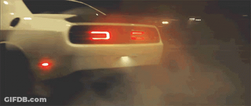 A White Car Is Driving Down A Street At Night GIF