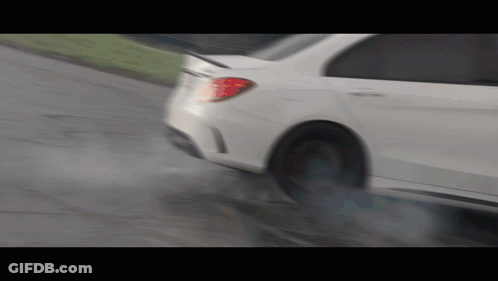 A White Car Is Driving Down A Wet Road With Smoke Coming Out Of The Tire GIF