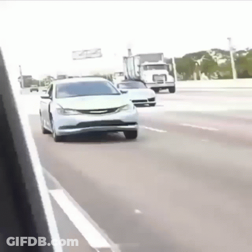 A White Car Is Driving Down The Highway Next To A Truck . GIF