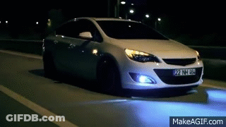A White Car Is Driving On A Highway At Night . GIF