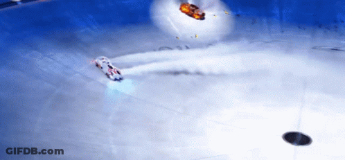 A White Car Is Driving On A Snowy Surface With A Red Car In The Background GIF