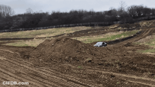 A White Car Is Driving Through A Dirt Field With A Fence In The Background GIF