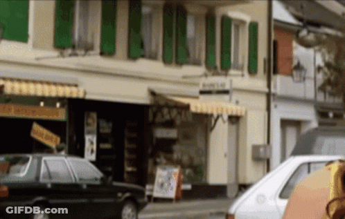 A White Car Is Parked In Front Of A Building That Has A Sign On It That Says ' A ' On It GIF