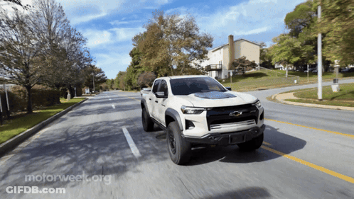 A White Chevrolet Truck Is Driving Down A Street GIF