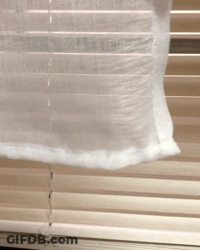 A White Curtain Is Hanging On A Window With Blinds GIF