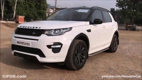 A White Discovery Is Parked On A Dirt Road GIF
