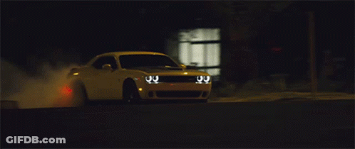 A White Dodge Challenger Driving Down A Street At Night GIF