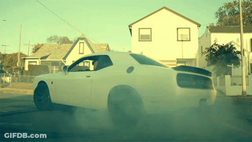 A White Dodge Challenger Is Driving Down The Street GIF