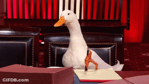 A White Duck Is Sitting At A Table With A Pen In Its Foot GIF
