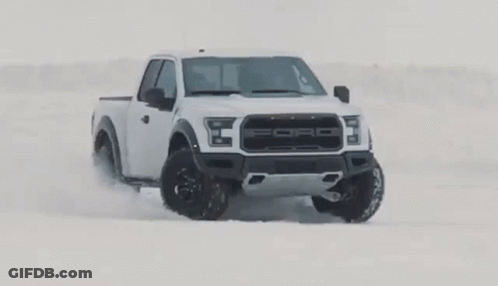 A White Ford Raptor Truck Is Driving In The Snow . GIF