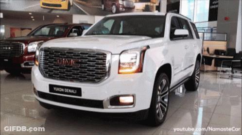 A White Gmc Yukon Denali Is Sitting In A Showroom GIF