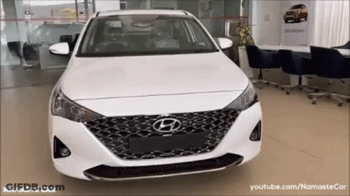 A White Hyundai Car Is Parked In A Showroom With The Words Namaste Car On The Bottom GIF