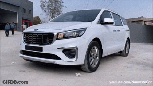 A White Kia Minivan Is Parked In A Parking Lot In Front Of A Building GIF