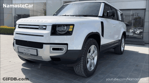A White Land Rover Defender Is Parked In Front Of A Namaste Car Dealership GIF