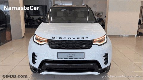 A White Land Rover Discovery Is Shown In A Showroom GIF