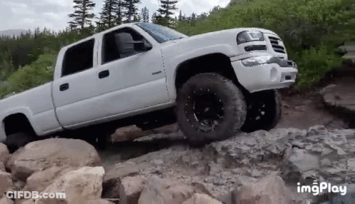 A White Pickup Truck Is Driving Down A Rocky Road . GIF