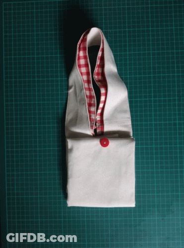 A White Piece Of Fabric With A Red And White Checkered Collar Is Sitting On A Green Cutting Board GIF