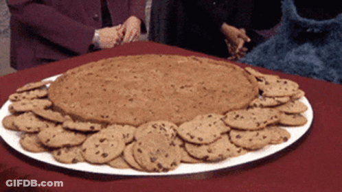 A White Plate Filled With Chocolate Chip Cookies And A Giant Cookie GIF