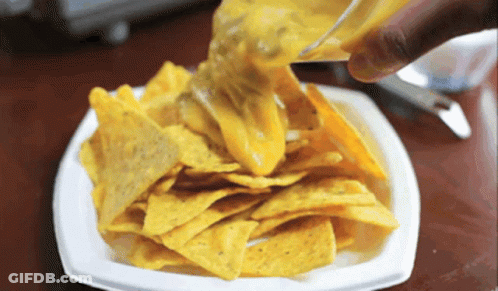 A White Plate Of Nachos With Cheese Being Poured On Top GIF